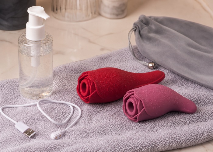 Rose-shaped vibrator with a charging cable, towel, and soft storage pouch on neutral bedding